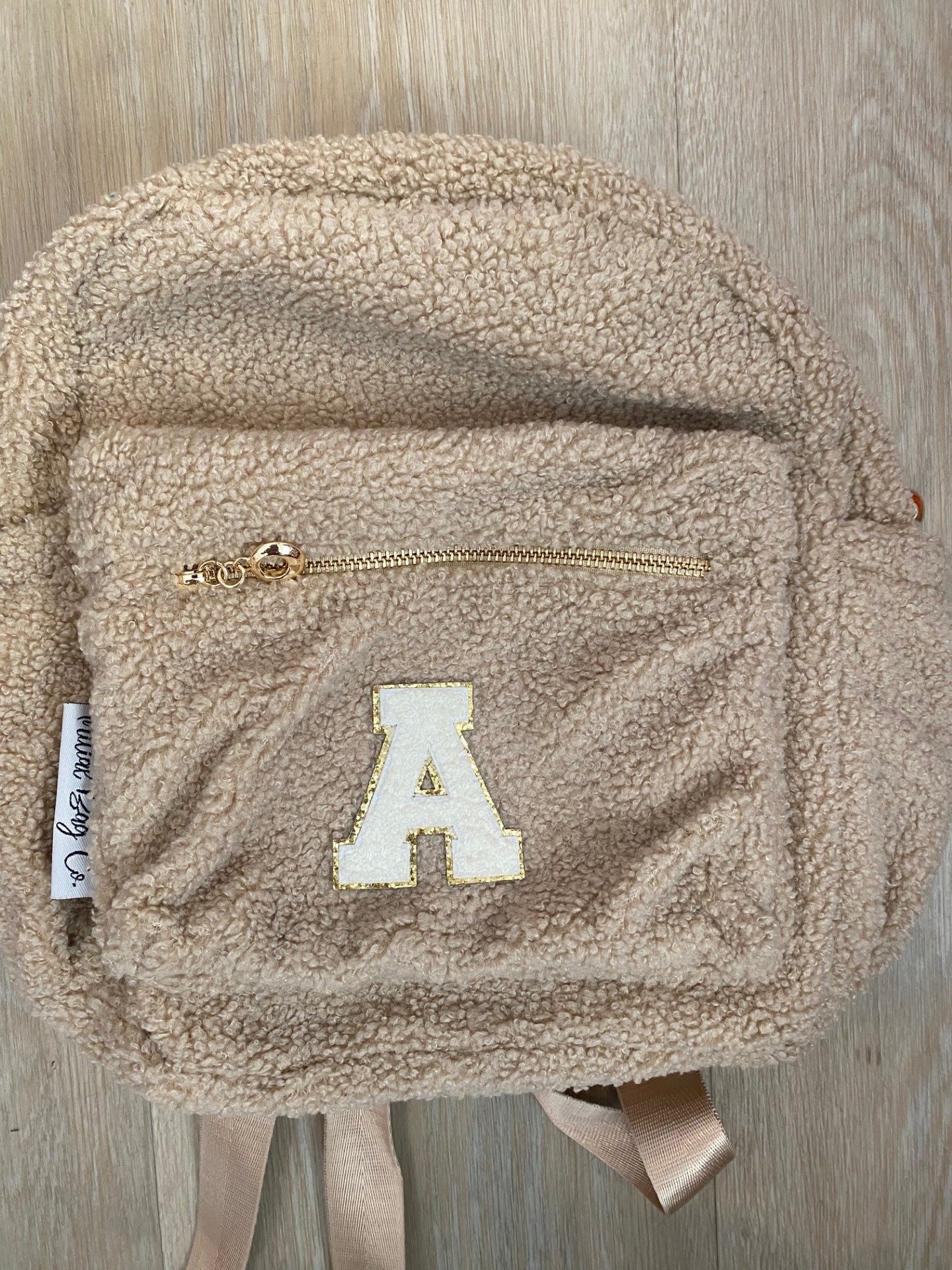 Beige backpack with initial "A" in white ** SLIGHT TEAR IN MATERIAL NEAR TOP ZIP**