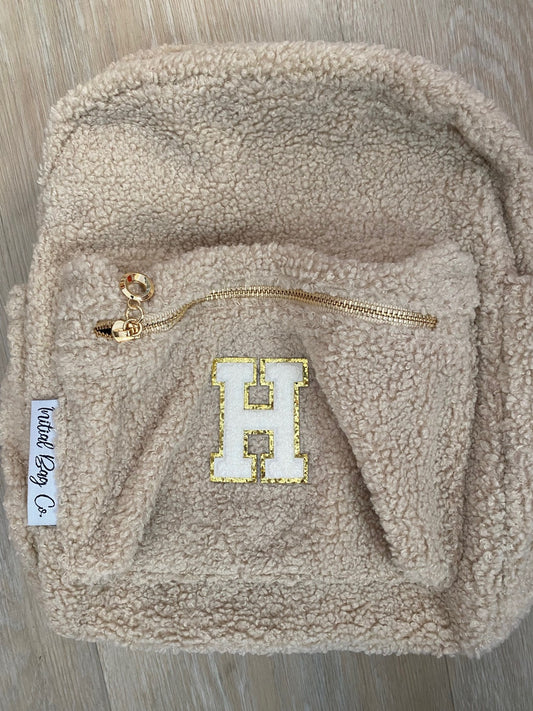 Beige backpack with initial 'H' in white **SLIGHT TEAR IN TOP MATERIAL**